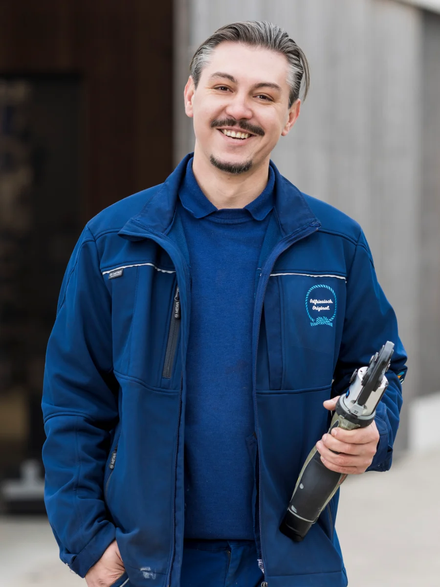 Lächelnder SHK-Mitarbeiter von Ubben SHK mit Werkzeug in der Hand vor einem Gebäude
